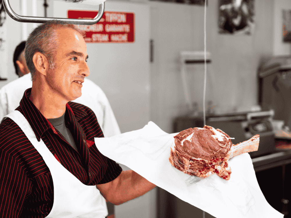Un boucher propose un morceau de viande à un client de la boucherie Sarthou à Lons